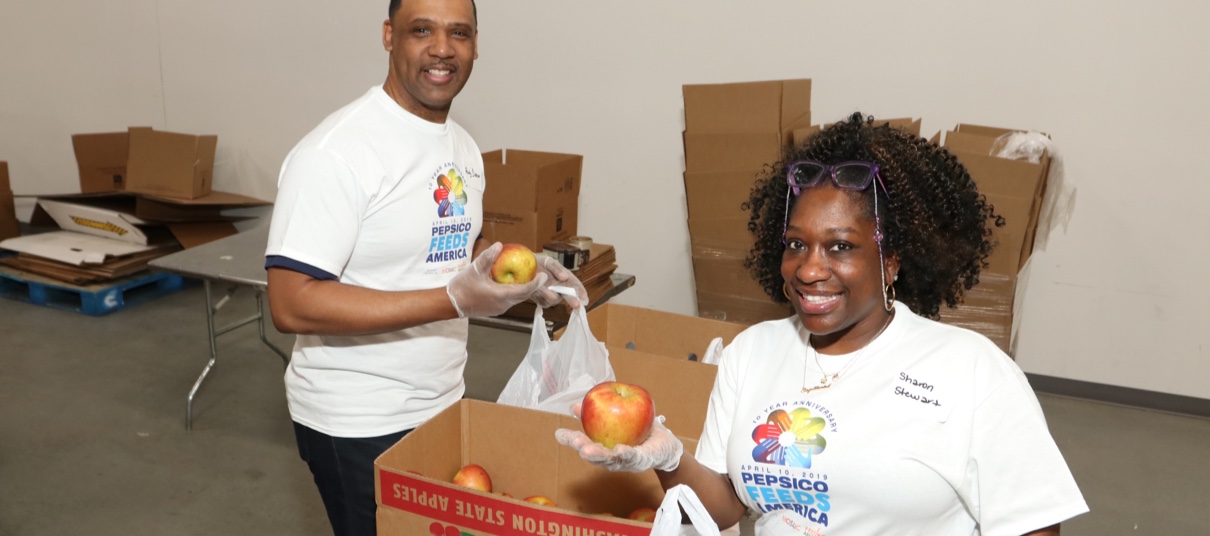 Two employees packing fruit into boxes while smiling at the camera