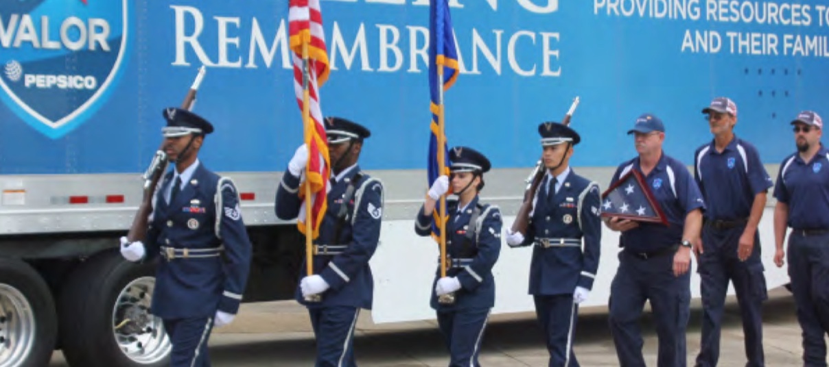 Four uniformed servicemen and women carrying two flags and leading procession
