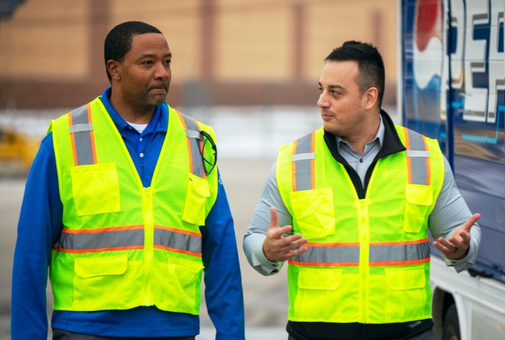Two men wearing bright yellow construction vests walking and talking
