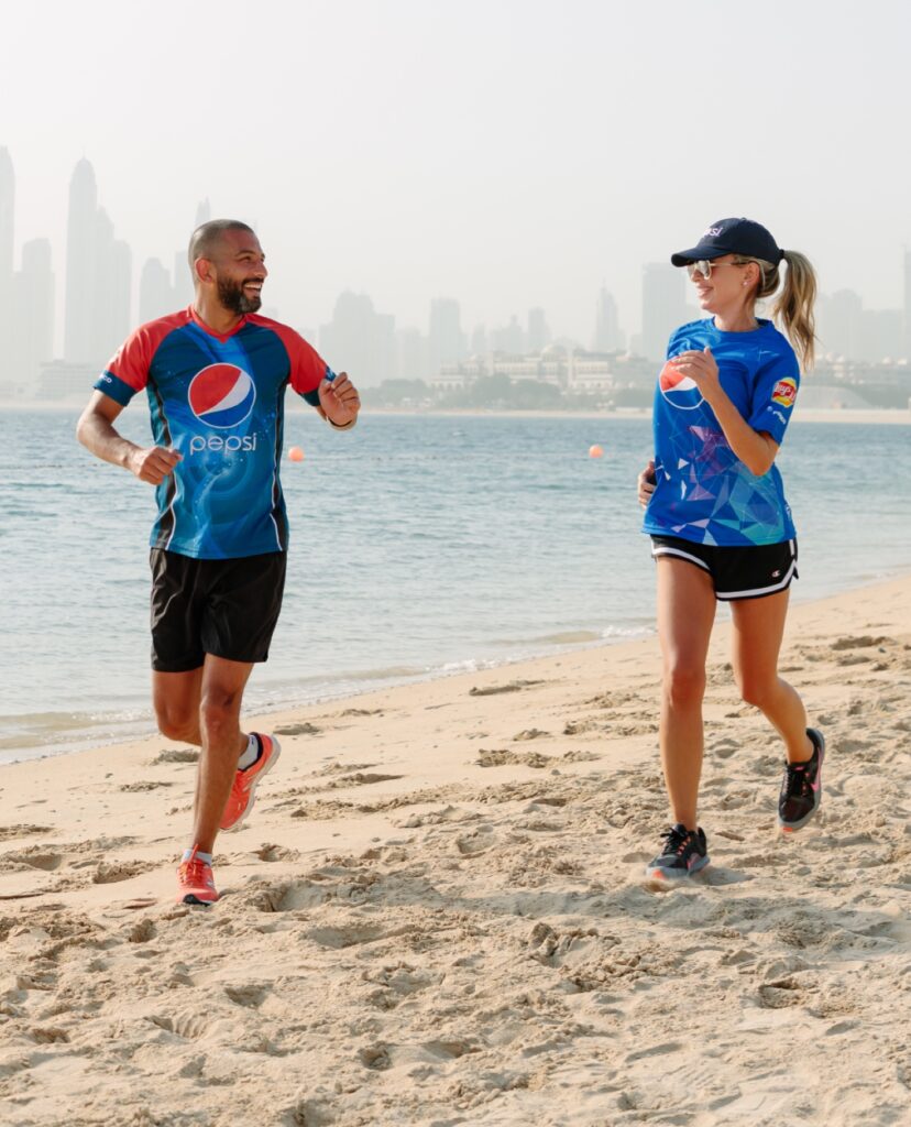 Two people wearing PepsiCo shirts jogging on a beach