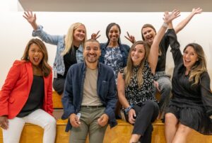 Group of seven people with arms up and smiling