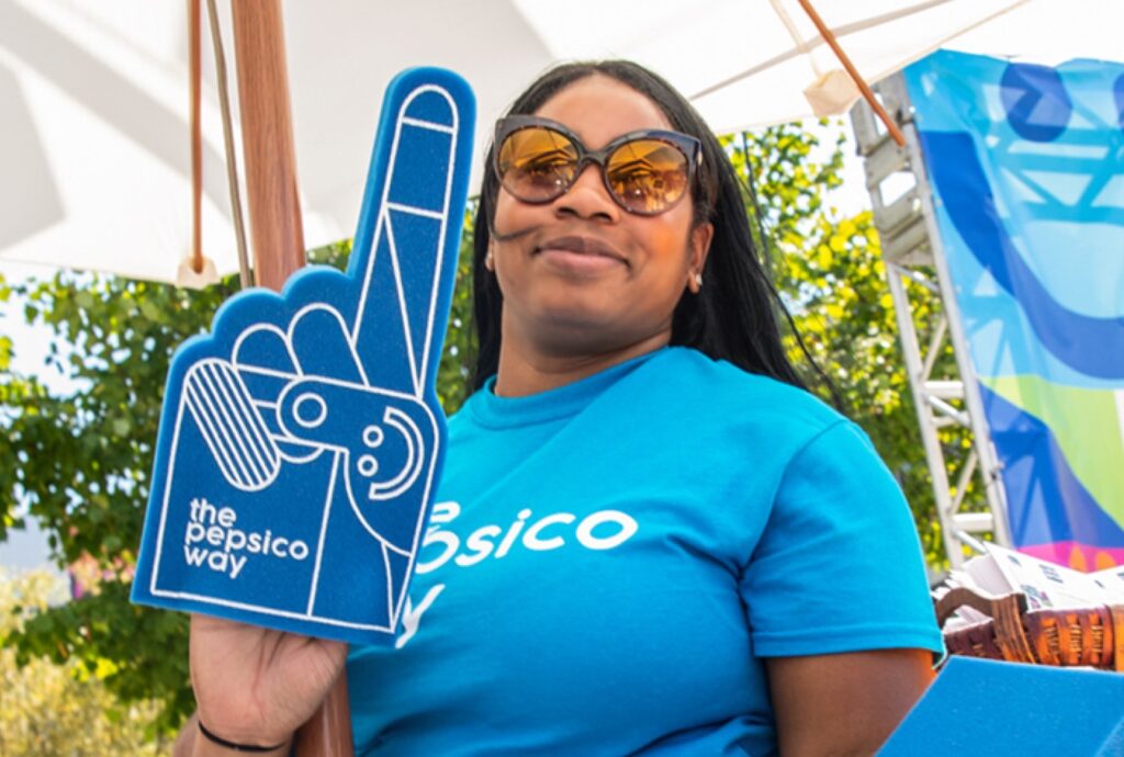 Woman wearing sunglasses and bright blue t-shirt holding PepsiCo blue foam finger