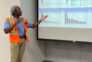 Man standing in front of and pointing at charts on a video projection screen